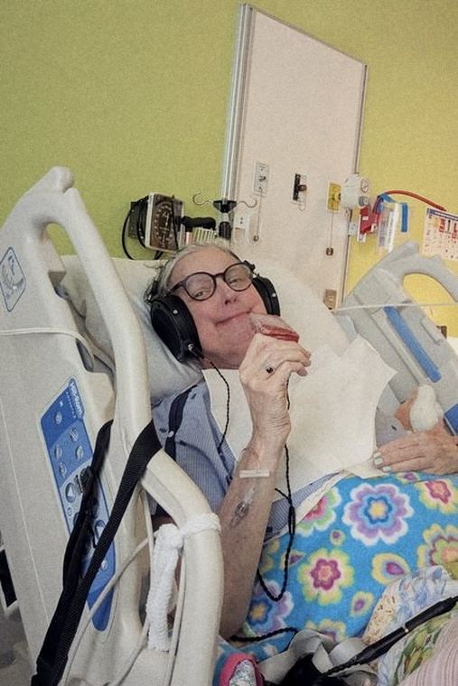 Josée dans un lit d'hôpital, grand casque d'écoute sur les oreilles, un popsicle rouge à la main.